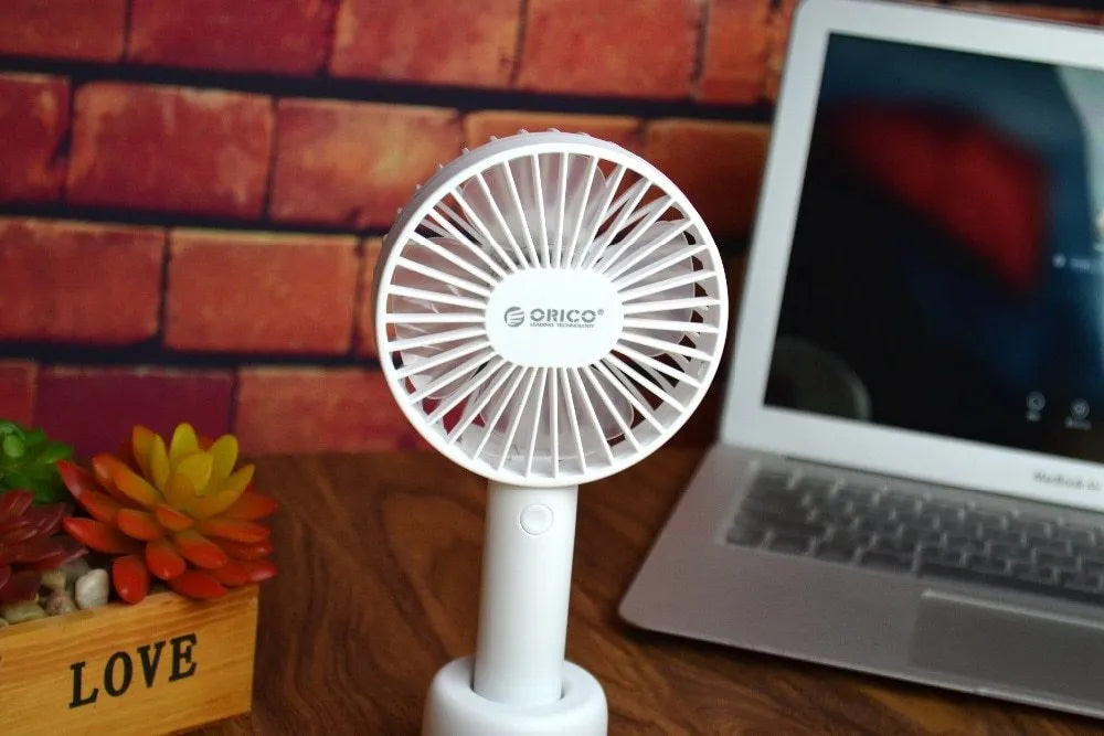 White ORICO FH1 handheld USB rechargeable desk fan with three-speed control on a desk.
