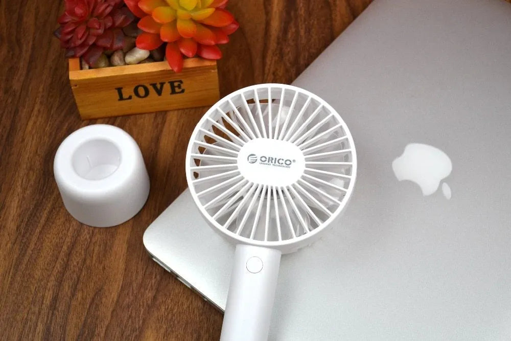 White ORICO FH1 handheld USB rechargeable desk fan with three-speed control on a desk.