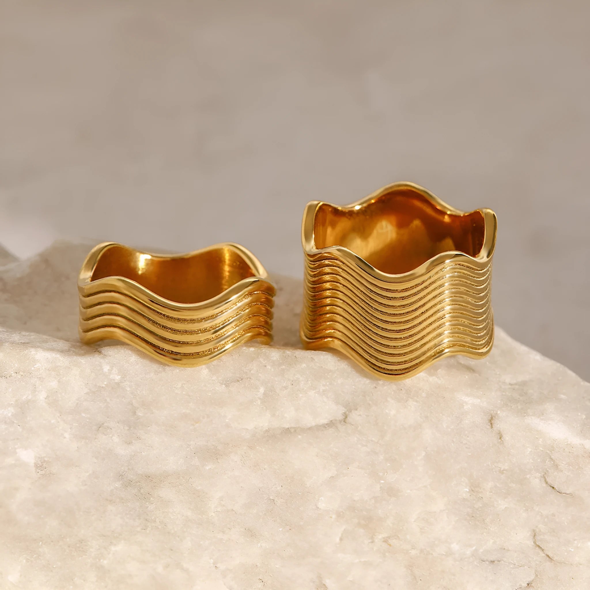 Close-up of a stainless steel ring with a wide geometric wave pattern and electroplated metallic finish.