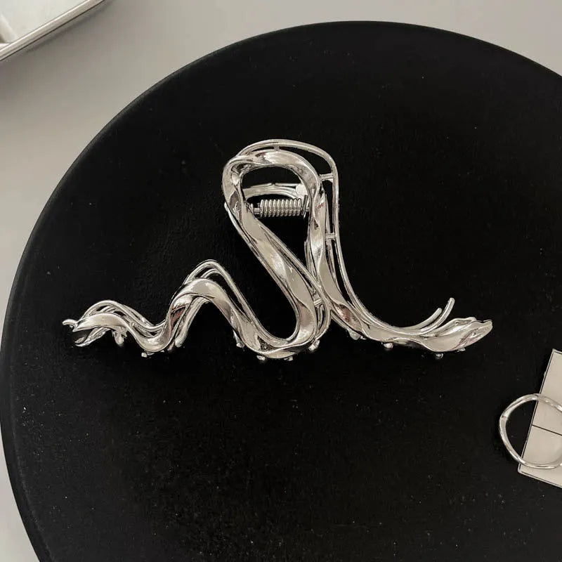 Assorted silver metal hair claws and barrettes including wave, knot, bow, and pearl designs on a white background.