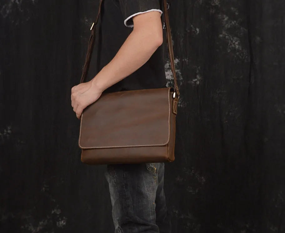 Men's vintage brown leather messenger bag with adjustable strap, shown open to reveal internal organiser pockets.