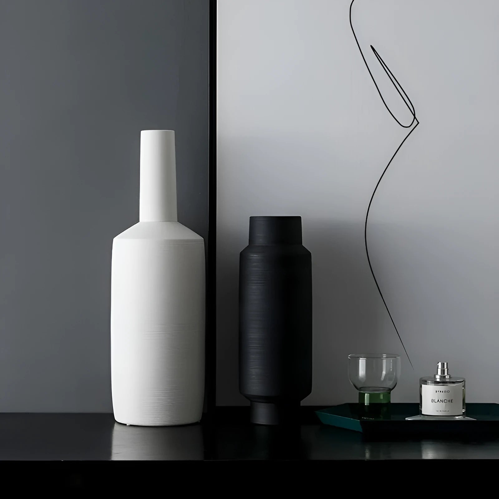 Three Nordic style ceramic vases with wire-drawn finish in neutral gray, black, and ivory white on a wooden table.
