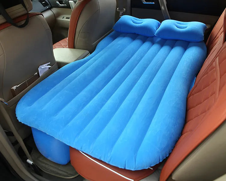 Black inflatable car bed with flocked surface set up in the back of a five-seater vehicle with pillows.