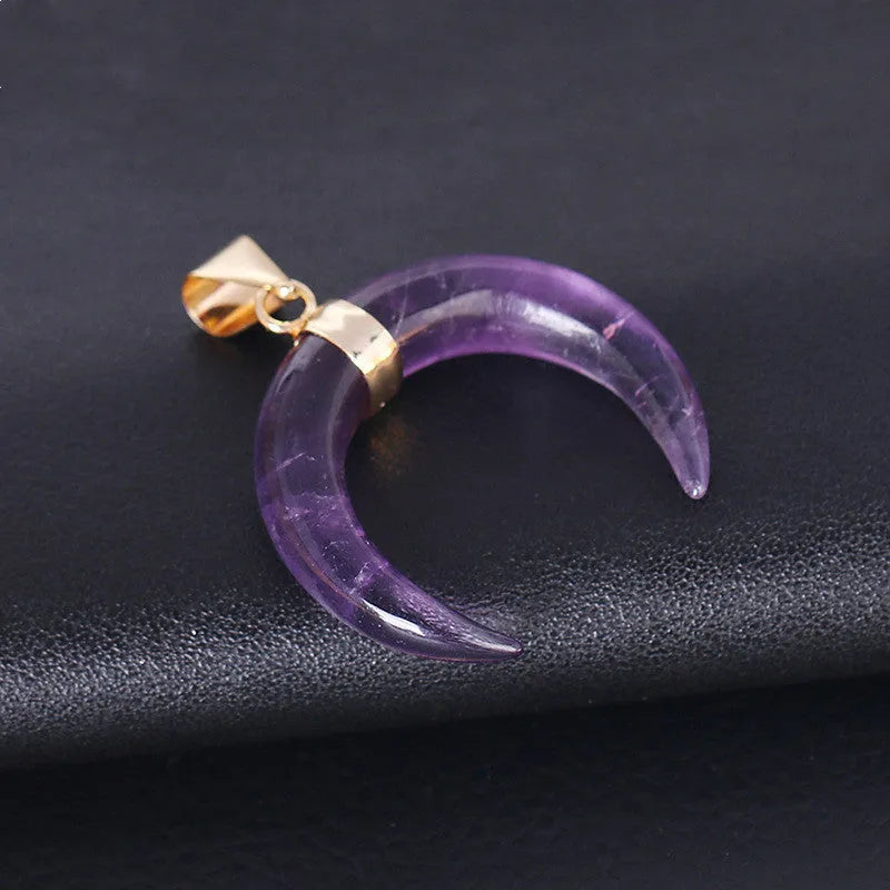 Close-up of a moon pendant necklace with a pink natural stone, on a copper-coloured chain against a neutral background.