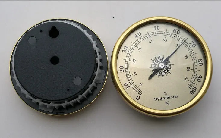 Analogue thermometer and hygrometer with aluminium dial on a white wall.