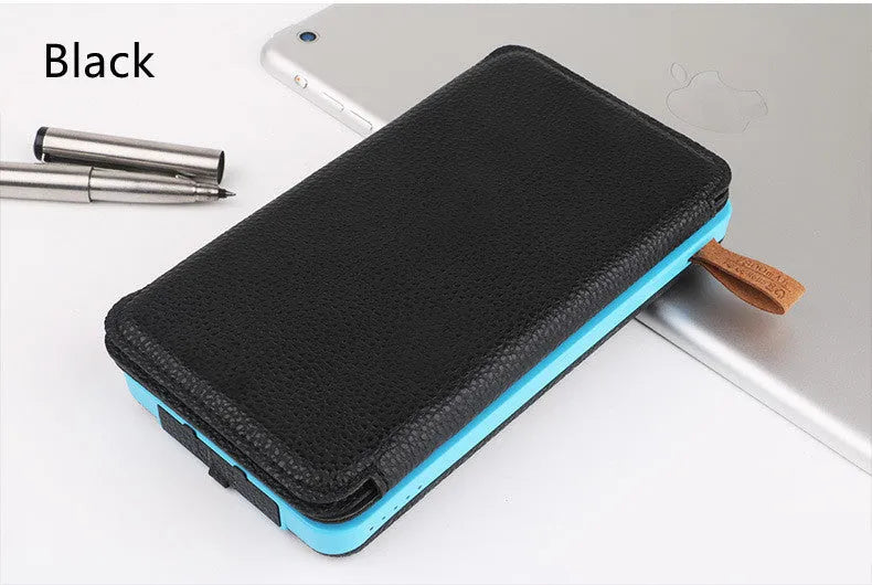 Black solar power bank with a solar panel, showing its USB ports and LED light, placed outdoors on a rock.