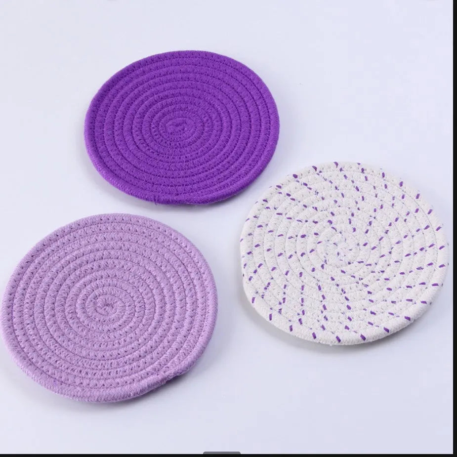 Set of three round grey cotton cord coasters on a wooden table.