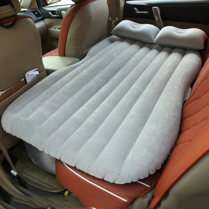 Black inflatable car bed with flocked surface set up in the back of a five-seater vehicle with pillows.