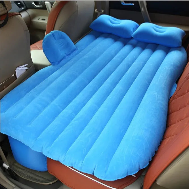 Black inflatable car bed with flocked surface set up in the back of a five-seater vehicle with pillows.