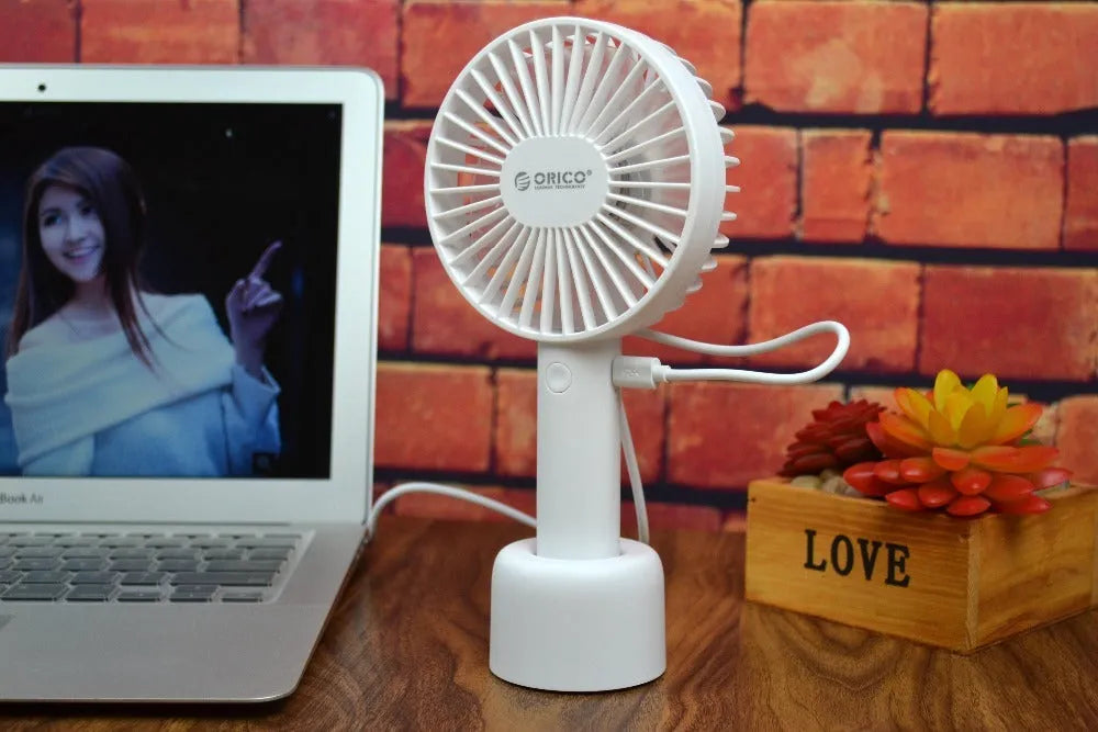 White ORICO FH1 handheld USB rechargeable desk fan with three-speed control on a desk.