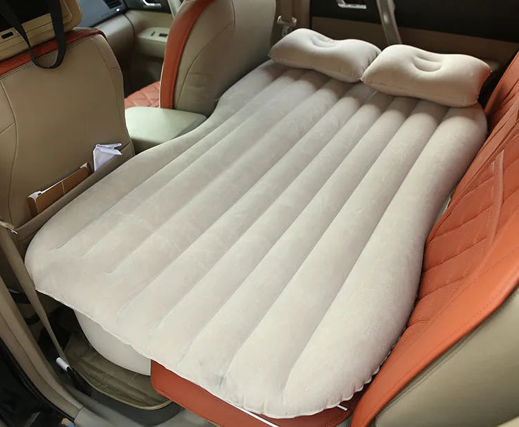 Black inflatable car bed with flocked surface set up in the back of a five-seater vehicle with pillows.