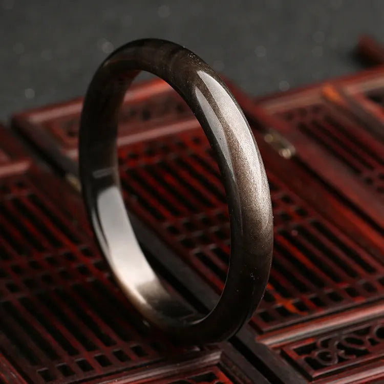 Natural silver stone cat's eye obsidian and alloy ethnic bracelet with geometric patterns on a wrist.