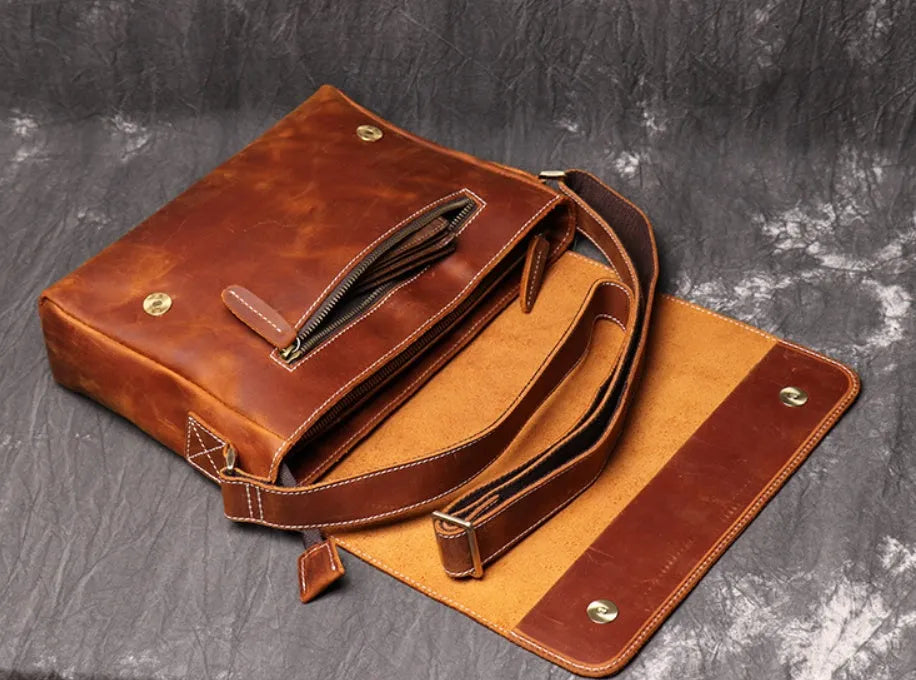 Men's vintage brown leather messenger bag with adjustable strap, shown open to reveal internal organiser pockets.