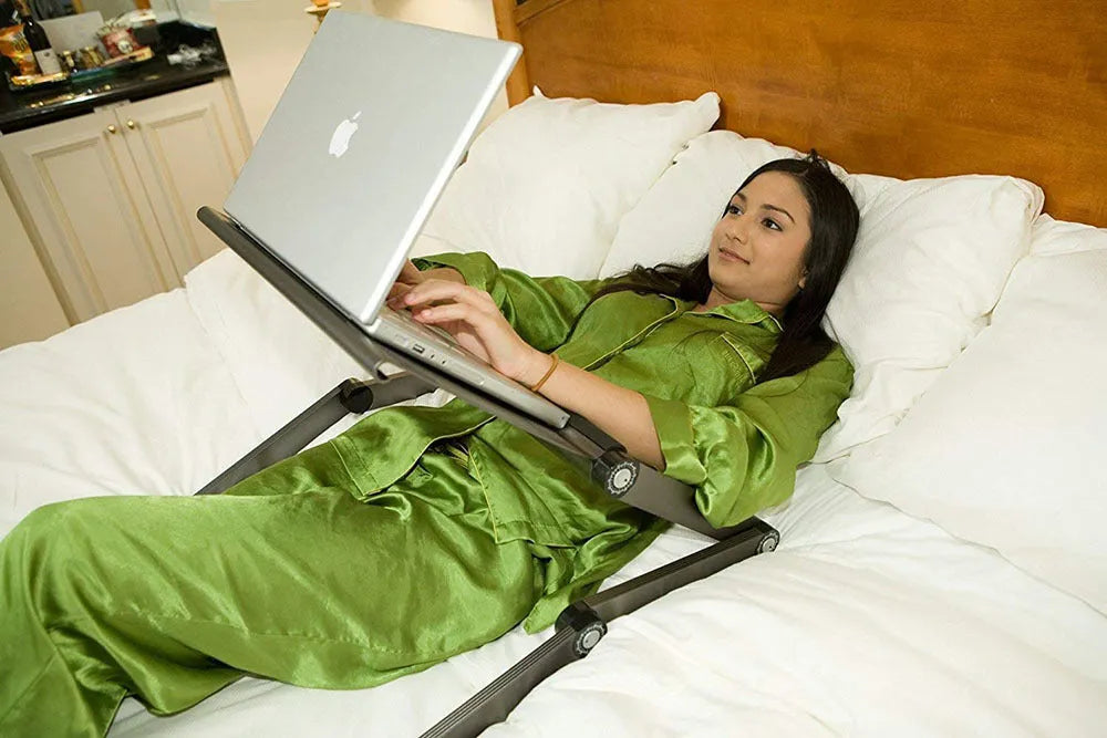 Adjustable black laptop stand desk with mouse pad and USB cooling fan, folded for storage, on a wooden floor