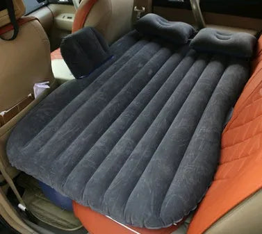Black inflatable car bed with flocked surface set up in the back of a five-seater vehicle with pillows.