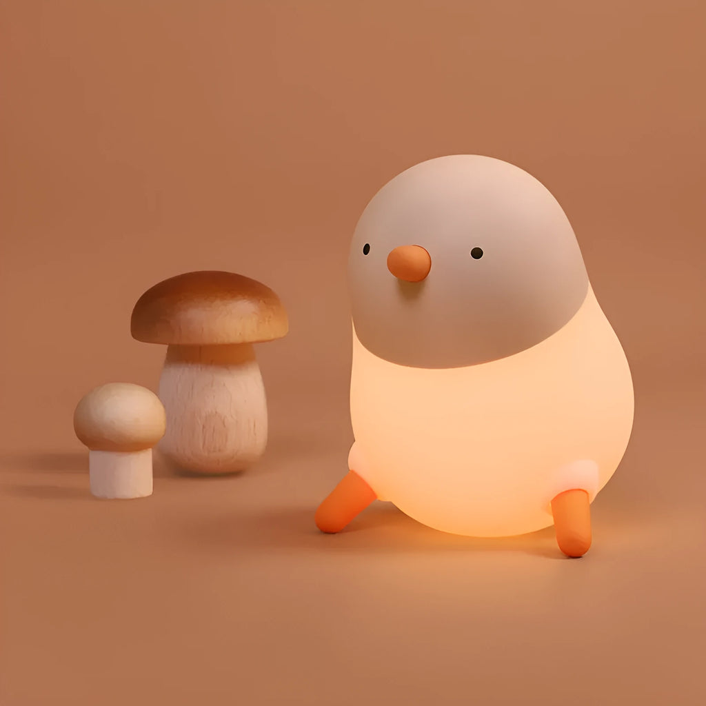 Pecking rice chicken small night light with warm yellow glow on a wooden bedside table, USB charging cable visible