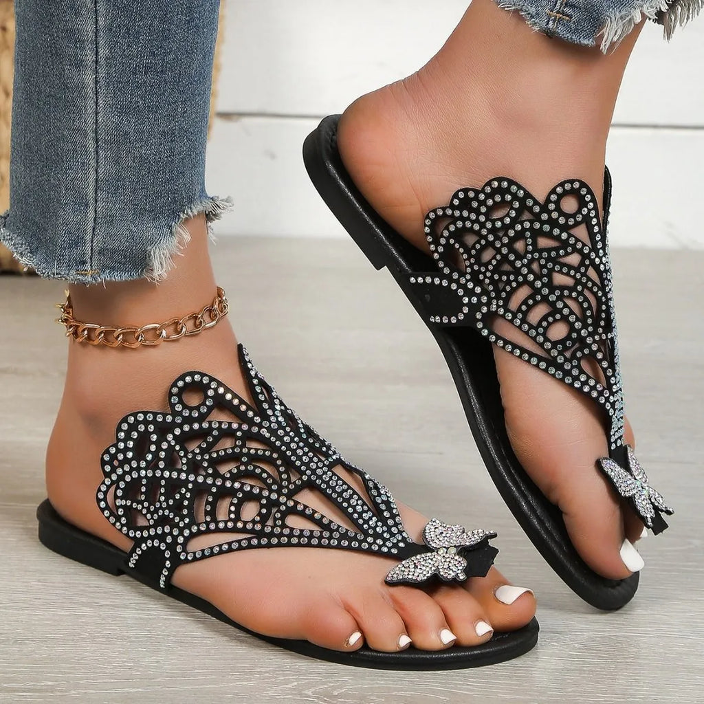 Women's black slip-on sandals with rhinestone accents and a hollow-out design on a flat rubber sole.