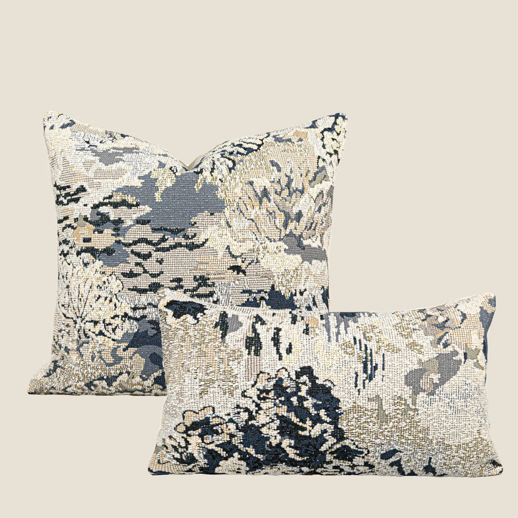Blue decorative pillow with abstract flower pattern in 50x50cm square size on a grey sofa.