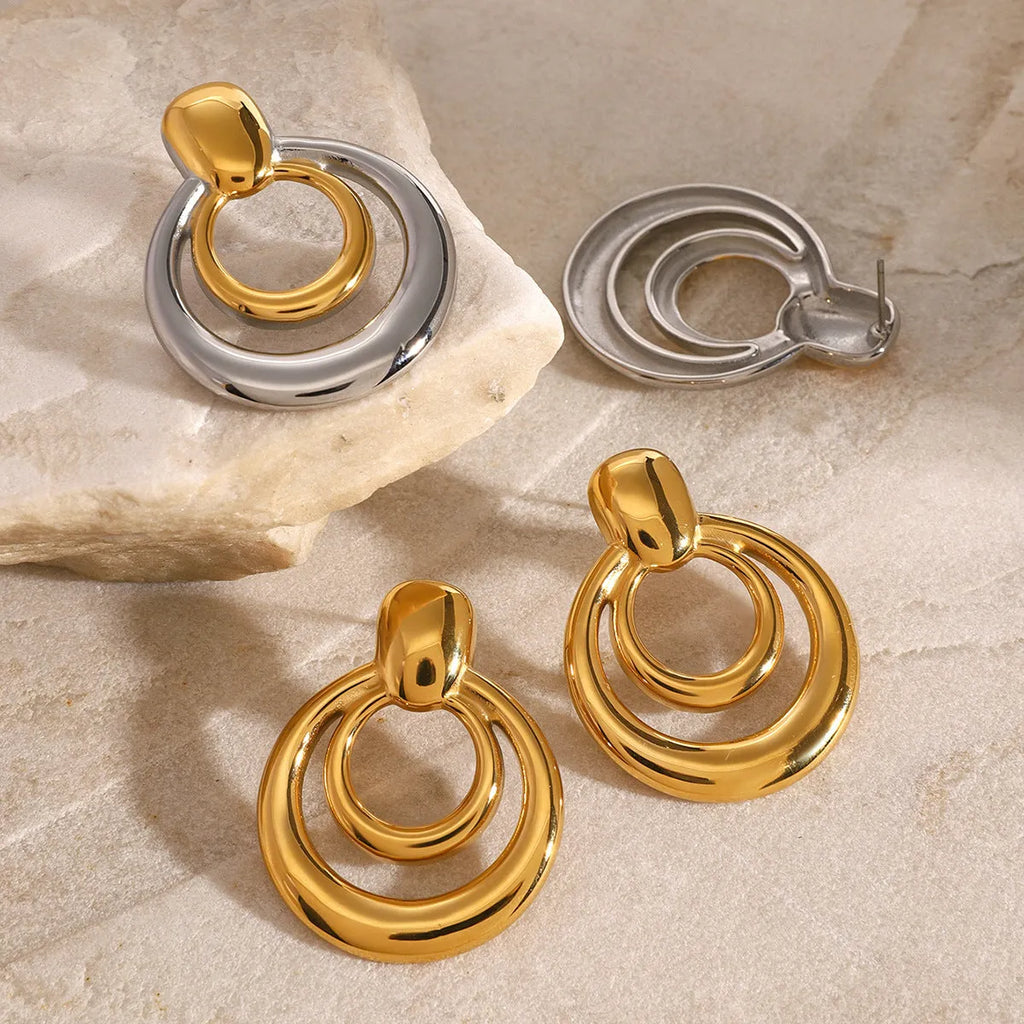 Close-up of a pair of round, geometric, double-layer hollow stud earrings with a golden electroplated finish.