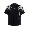 Black loose-fit short-sleeve t-shirt with padded shoulders featuring a decorative rivet and ribbon detail.