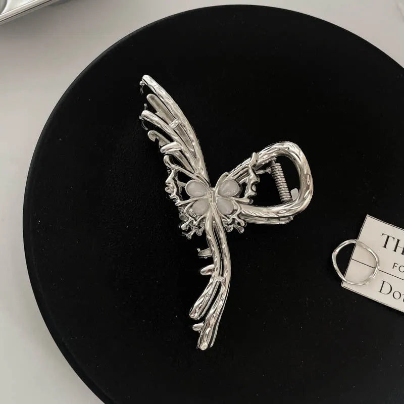 Assorted silver metal hair claws and barrettes including wave, knot, bow, and pearl designs on a white background.