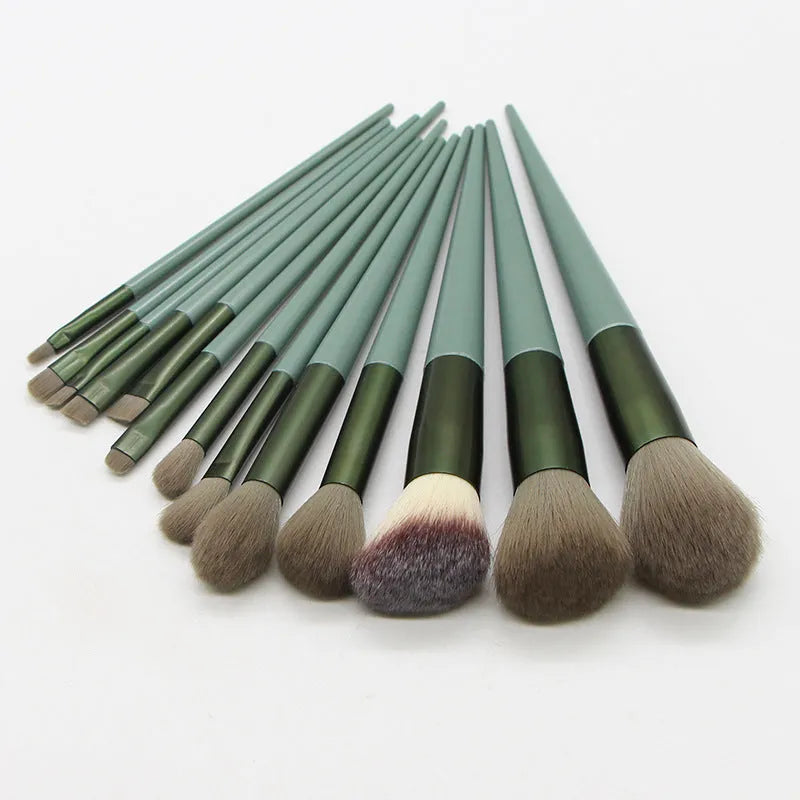 13 green makeup brushes with fibre wool bristles and aluminium tubes arranged on a surface