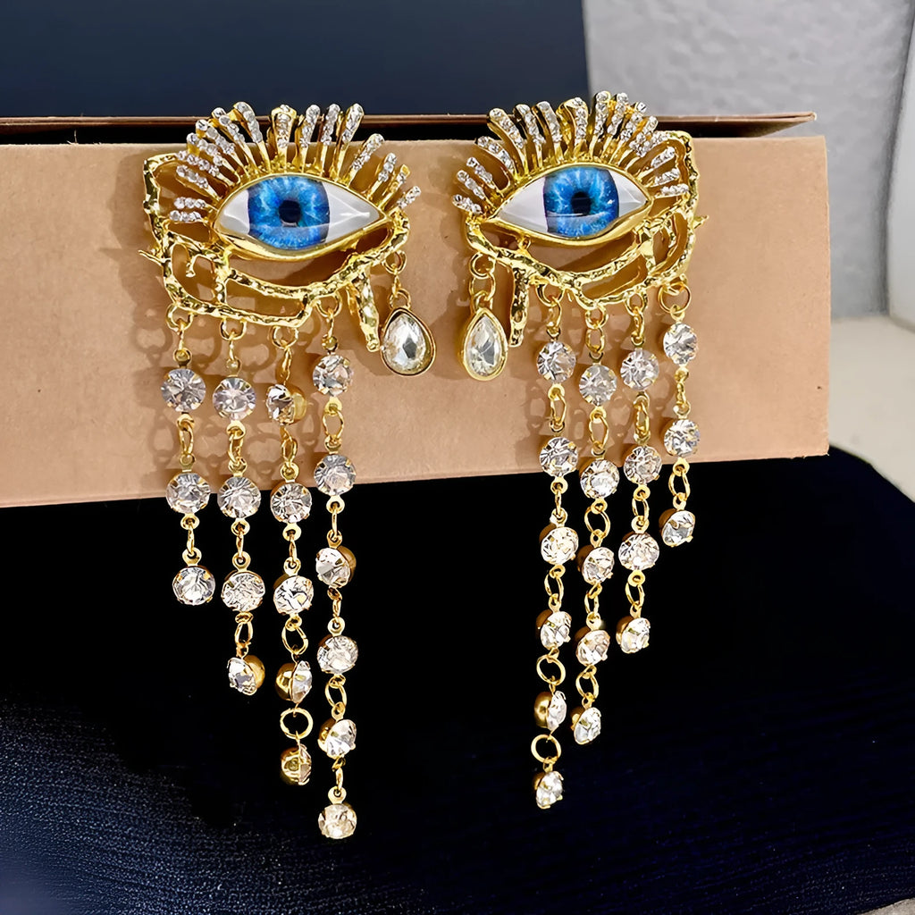 Pair of gold plated long tassel earrings with artificial crystal and zircon elements, eye motif, on white background
