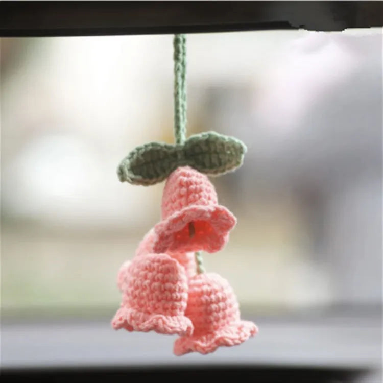 Green and white knitted wool car plant decoration with macramé texture and a white hanging rope.