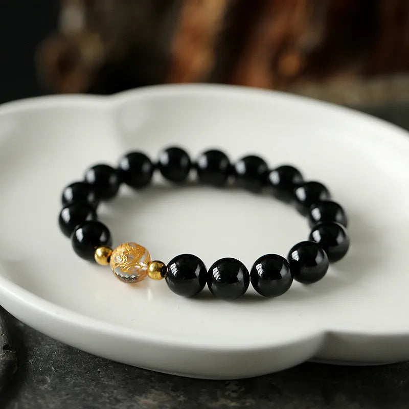 Geometric obsidian and white crystal beaded bracelet with golden dragon charm on a wrist.