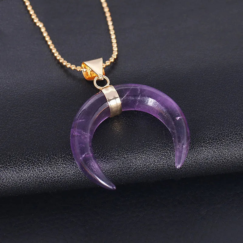 Close-up of a moon pendant necklace with a pink natural stone, on a copper-coloured chain against a neutral background.