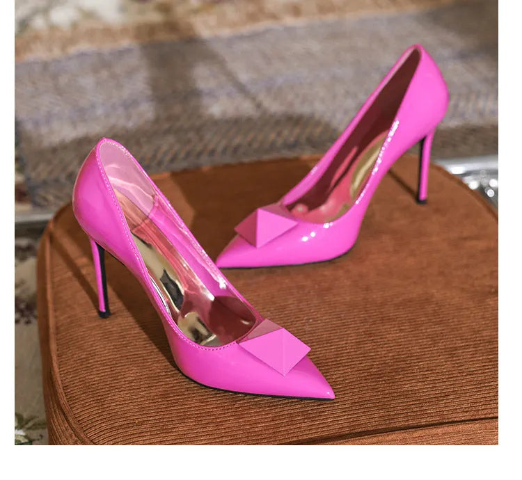 Women's pink patent leather pointed toe stiletto heels with buckle closure and rivet details