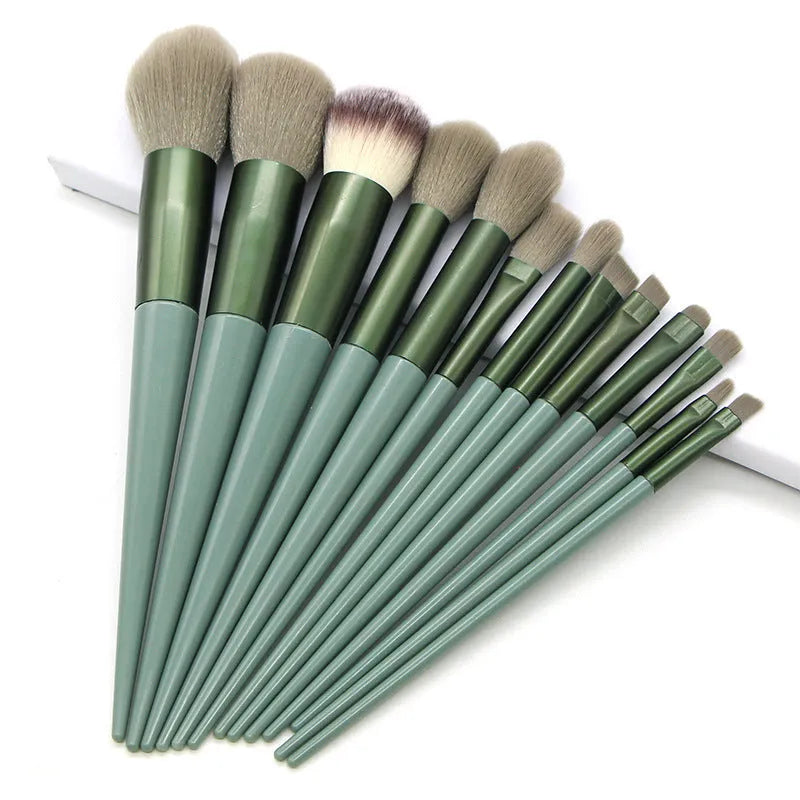 13 green makeup brushes with fibre wool bristles and aluminium tubes arranged on a surface