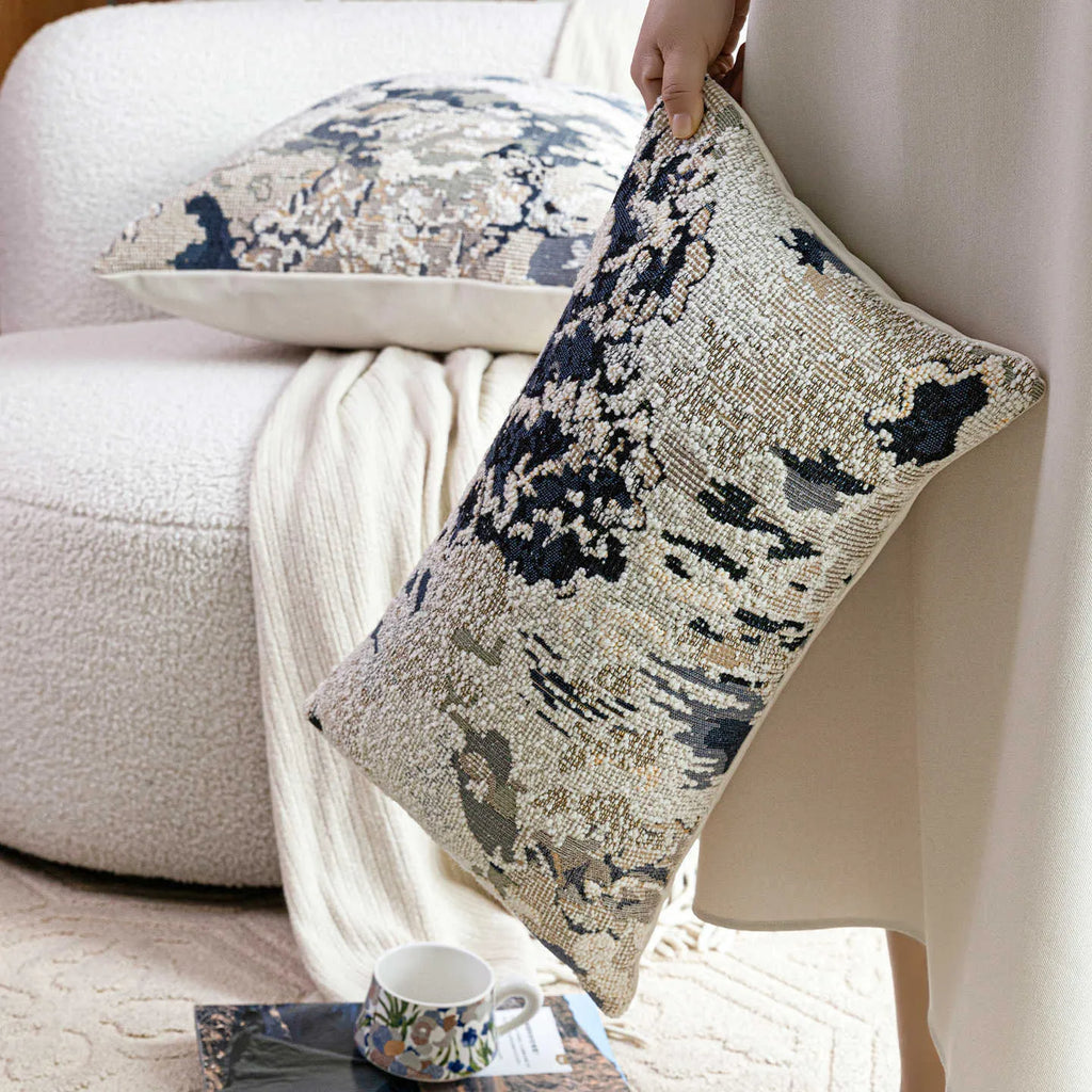 Blue decorative pillow with abstract flower pattern in 50x50cm square size on a grey sofa.