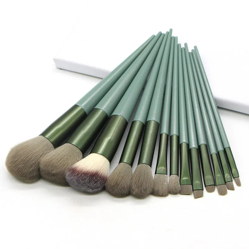 13 green makeup brushes with fibre wool bristles and aluminium tubes arranged on a surface