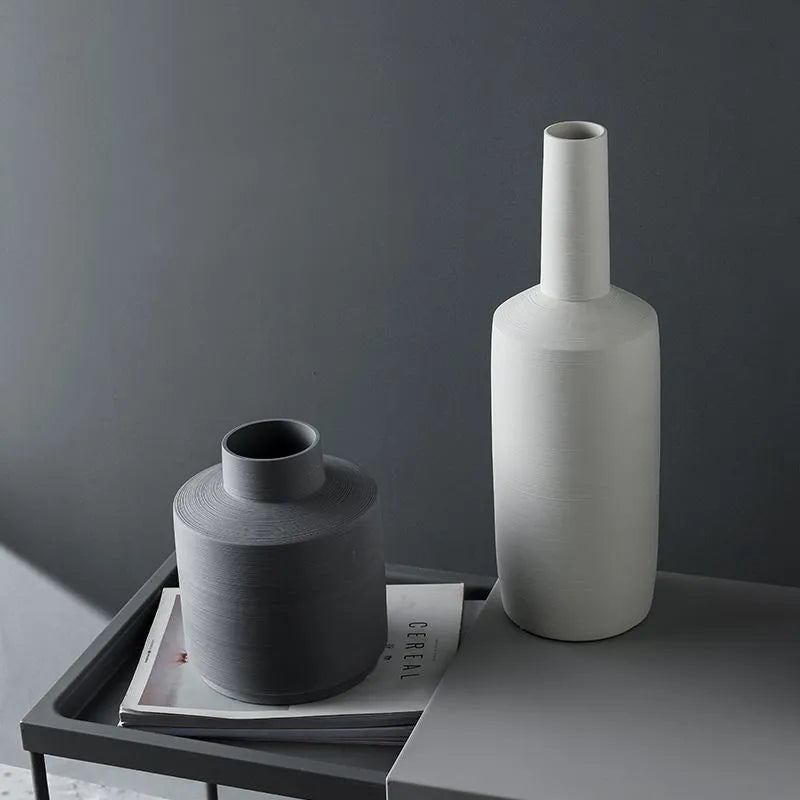 Three Nordic style ceramic vases with wire-drawn finish in neutral gray, black, and ivory white on a wooden table.