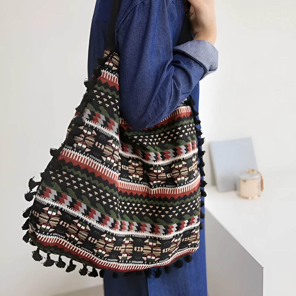 Green geometric tribal tasselled tote bag with oval shape, open top, and two handles, shown on a flat surface
