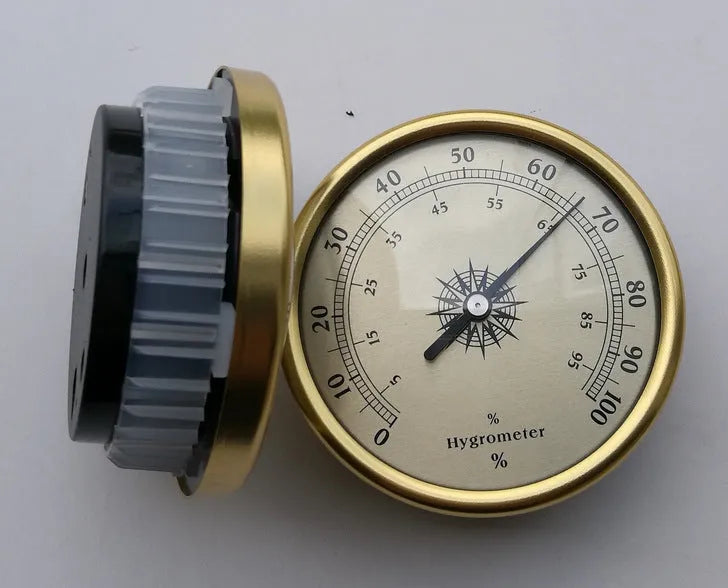 Analogue thermometer and hygrometer with aluminium dial on a white wall.