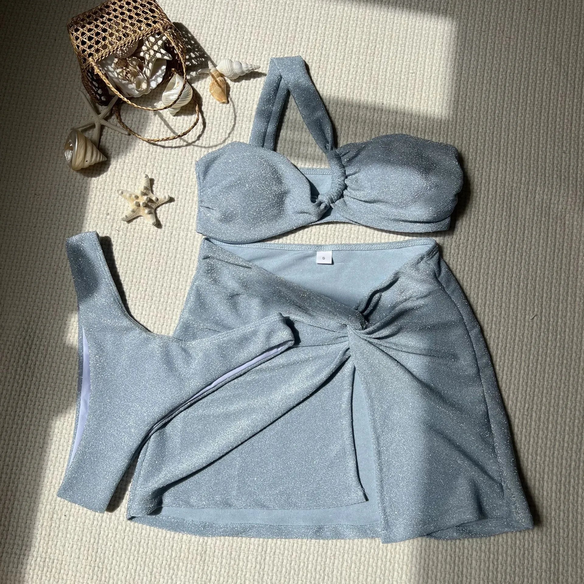 Women's light green one-shoulder swimsuit top with matching skirt and pants on a hanger.