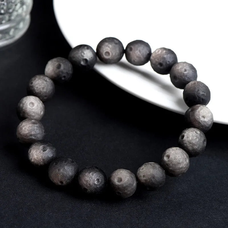 Natural obsidian crater ball bracelet with meteorite-like texture in silver stone or gold finish.