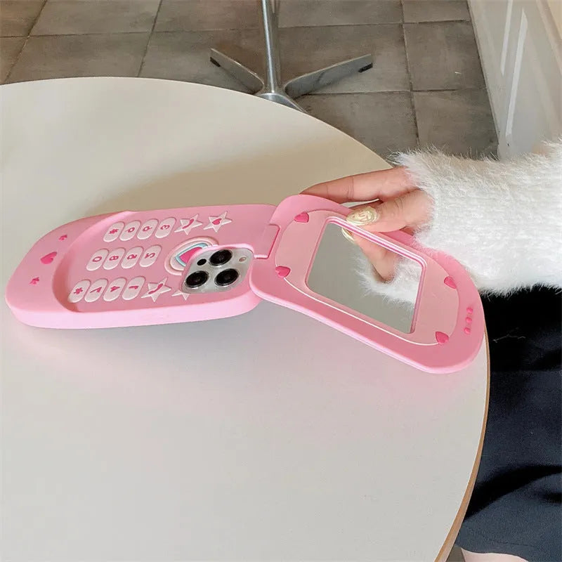 Pink silicone iPhone case shaped like a flip phone with a built-in mirror, showing cute cartoon style.