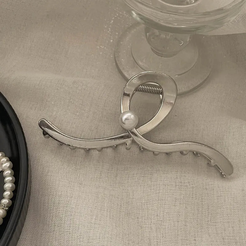 Assorted silver metal hair claws and barrettes including wave, knot, bow, and pearl designs on a white background.