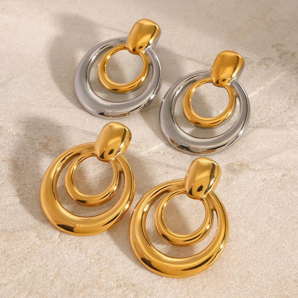 Close-up of a pair of round, geometric, double-layer hollow stud earrings with a golden electroplated finish.