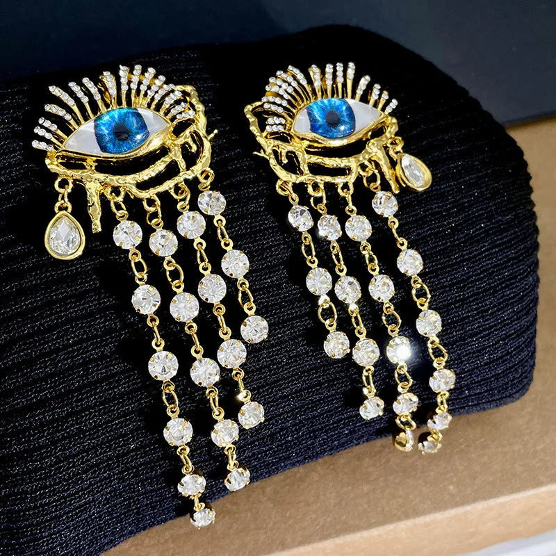Pair of gold plated long tassel earrings with artificial crystal and zircon elements, eye motif, on white background