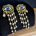 Pair of gold plated long tassel earrings with artificial crystal and zircon elements, eye motif, on white background