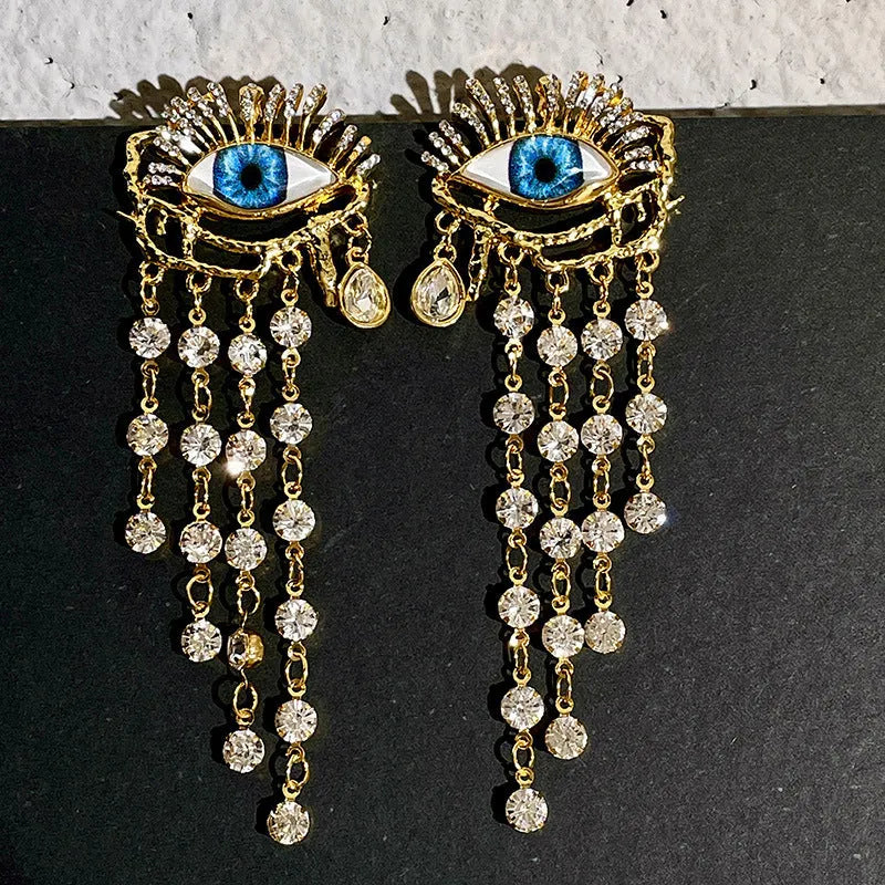 Pair of gold plated long tassel earrings with artificial crystal and zircon elements, eye motif, on white background