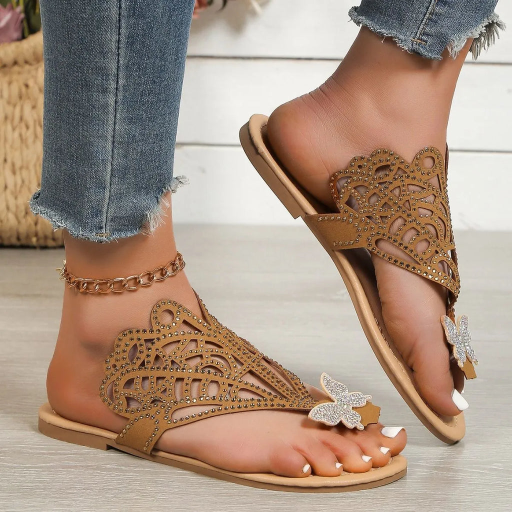 Women's black slip-on sandals with rhinestone accents and a hollow-out design on a flat rubber sole.