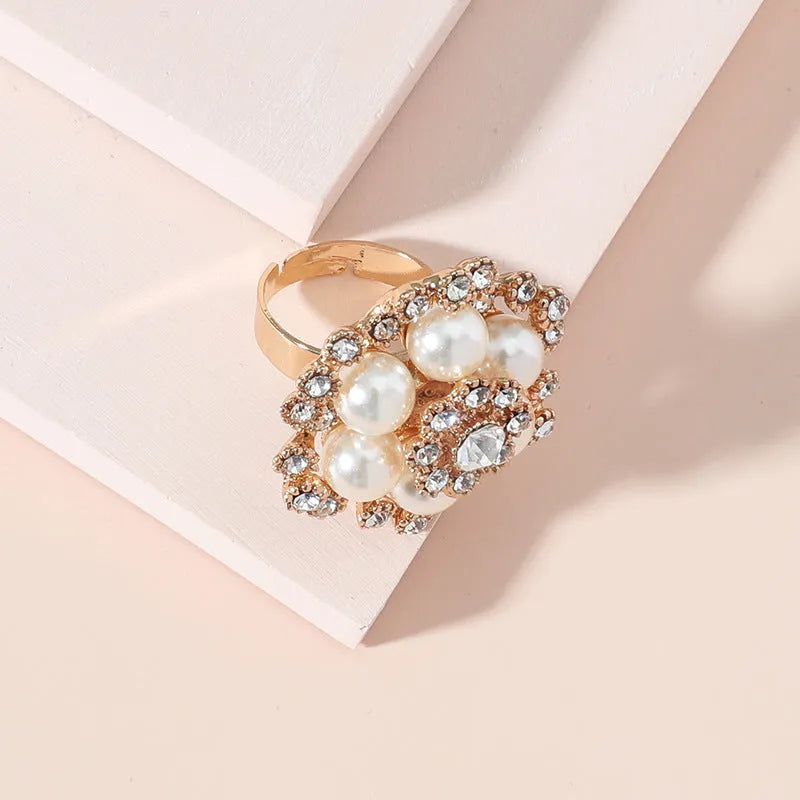 Simple retro fashion ring with pearl inlay and rhinestone flower shape in white KC gold on a flat surface