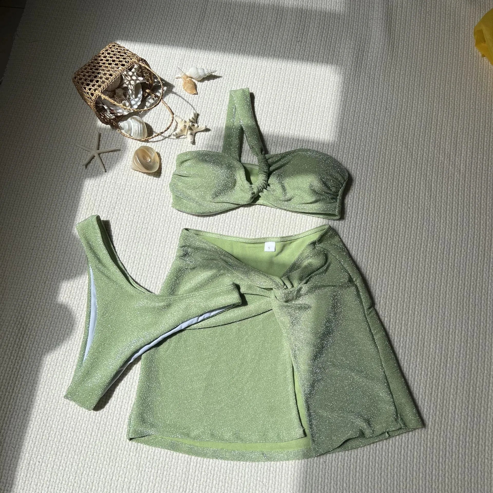 Women's light green one-shoulder swimsuit top with matching skirt and pants on a hanger.