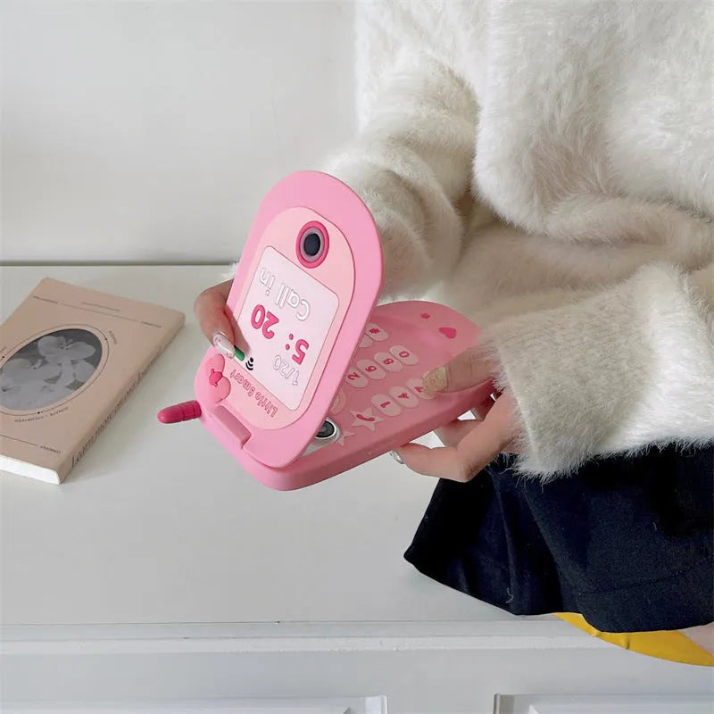 Pink silicone iPhone case shaped like a flip phone with a built-in mirror, showing cute cartoon style.