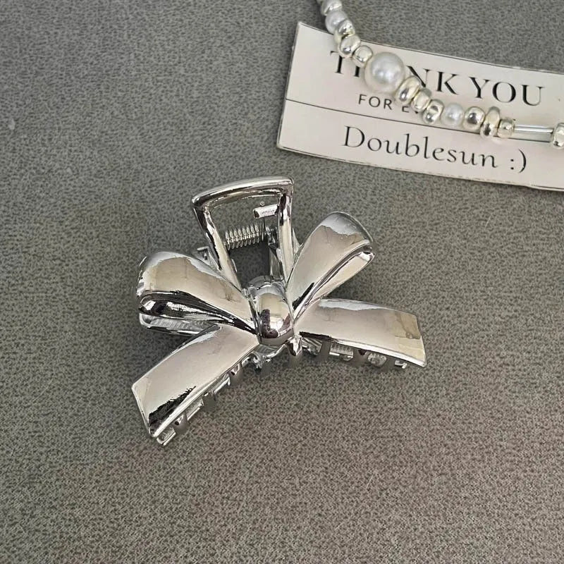 Assorted silver metal hair claws and barrettes including wave, knot, bow, and pearl designs on a white background.